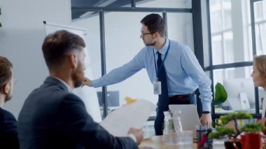 Profesyonel bir adam, kurumsal bir ofis ortamında toplanmış çeşitli kişilere ilgi çekici bir sunum sunuyor.