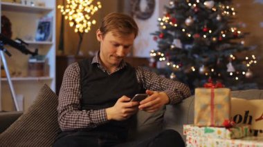 Kız arkadaşıyla konuşan, kanepede oturan genç, tatlı bir adam. Bir kız için hediye gösteren bir adam, video araması yapıyor. Gülümsüyor. Noel atmosferi.