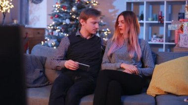 Kafkasyalı genç bir çift, güzel bir oturma odasında topları ve ışıklarıyla süslenmiş Noel ağacıyla kavga ediyor. Akıllı telefonu saklayan güzel kız. Gençler gülüyor. Kapalı.