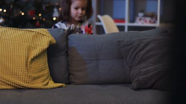 Koltuğun arkasından koltuğun altında yumuşak köpek oyuncağıyla görünen kız. Sevimli küçük hanım hediyesini kanepeye koyup tekrar saklanıyor..