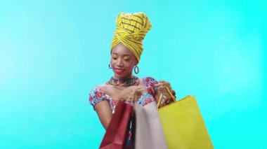 Şık giyinmiş şık bir kadın, parlak bir arka planda alışveriş çantalarını rahatça sergiliyor.