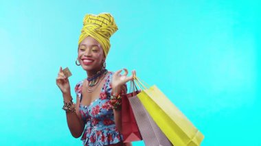 Renkli elbiseli şık bir kadın canlı bir arka planda alışveriş torbalarını neşeyle sergiliyor.