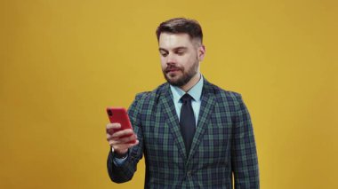 Şık bir iş adamı akıllı telefonuyla aktif olarak meşgul, çarpıcı derecede canlı sarı bir arkaplanda yakalandı.