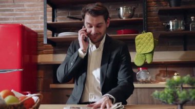 Takım elbiseli iyi giyimli bir adam şık bir mutfakta oturur, gazete okur ve taze meyvelerle çevrilidir.