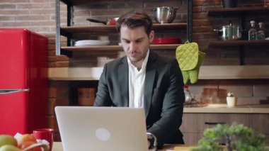 Kendini işine adamış bir işadamı, canlı dekorlarla dolu şık bir mutfakta otururken dizüstü bilgisayarına odaklanmış.