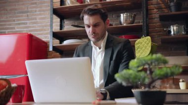 Kendini işine adamış ve işine odaklanmış bir profesyonel şık ve modern bir mutfakta dizüstü bilgisayarda üretken bir iş yapıyor.