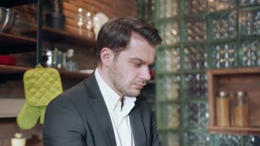 Profesyonel takım elbiseli, çok odaklanmış bir adam, şık bir mutfak ortamında yoğun bir şekilde çalışıyor.