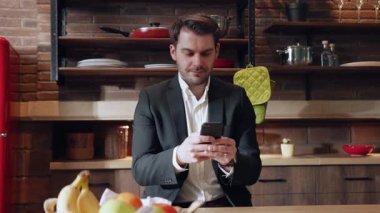 Şık ve modern bir mutfak ortamında, profesyonel bir adam telefonuyla mesajlaşır, çoklu görev tanıtımı yapar.