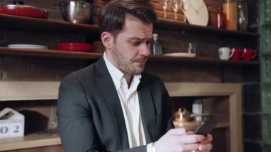 Bir işadamı, şık ve modern bir mutfak ortamında akıllı telefonunu dikkatli bir şekilde kullanırken oldukça endişeli görünüyor.