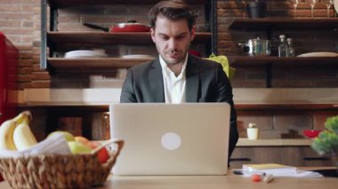 Odaklanmış bir işadamı, yaratıcılığa ilham veren şık ve modern bir mutfakta özenle dizüstü bilgisayarı üzerinde çalışır.