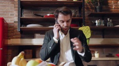 Bir iş adamı, şık ve modern bir mutfakta dururken telefonla konuşur.