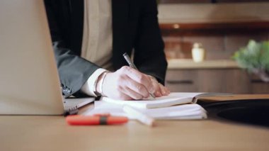 Odaklanmış bir birey dizüstü bilgisayar kullanırken bir deftere yazarak üretkenliğe ve planlamaya bağlılığını gösterir.