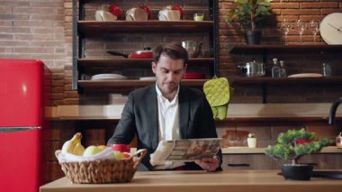 Şık bir mutfakta oturmuş neşeyle gazete okurken sabah rutininden zevk alan bir işadamı.