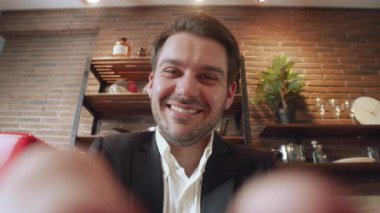 Takım elbise giymiş gülümseyen bir adam sıcak ve davetkar bir kafe atmosferinde keyifli bir anın tadını çıkarır.