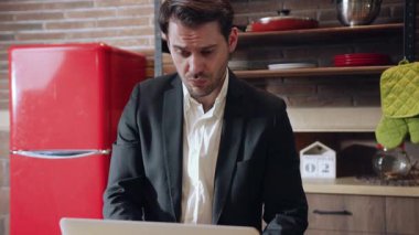 İş elbisesi giymiş bir adam şık bir mutfak ortamında dizüstü bilgisayarına odaklanır.