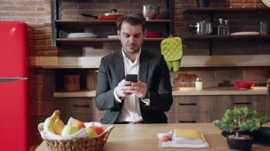Modern ve şık bir mutfakta, bir iş adamı akıllı telefonuyla derinden ilgilenir, işine odaklanır.