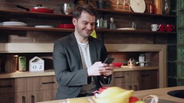 Bir adam akıllı telefonuyla modern, şık bir mutfakta, etrafında bir dizi taze meyve ile meşgul.