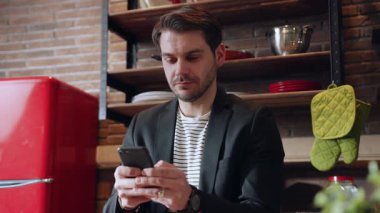 Genç bir profesyonel, şık bir mutfak ortamının ortasında akıllı telefonuyla derinden ilgilenir.