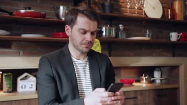 Profesyonel bir adam, şık ve çağdaş bir mutfak ortamında akıllı telefonuyla aktif olarak meşgul olur.