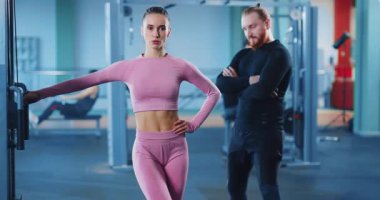Güçlü genç sporcu kadın bacak kaldırma egzersizi yapıyor dayanıklılık egzersizi yapıyor modern spor kulübünün iç kısımlarında kişisel koçla antrenman yapıyor. Oyunculuk sporu.