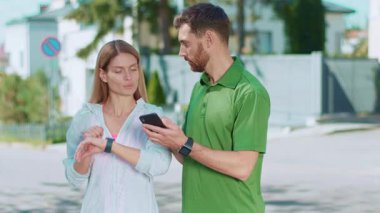 Bir çift, doğa ile dolu canlı bir açık hava ortamında akıllı telefon ve akıllı saatle iletişim kuruyor.