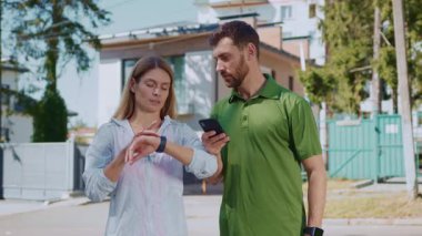 Bir erkek ve bir kadın dışarıda eğlenirken spor takip cihazlarını kontrol ediyorlar.