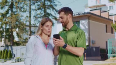 Akıllı bir telefonla meşgul olan bir çift, açık havada canlı bir ortamda spor ipuçlarını neşeyle paylaşıyorlar.