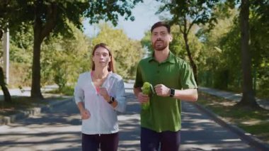 Bir çift, yemyeşil bir parkta birlikte koşmaktan zevk alarak spor yapmayı ve sağlıklı yaşam alışkanlıklarını teşvik ediyor.