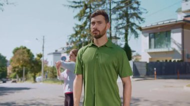 Yeşil tişörtlü bir adam güzel ve açık bir günde banliyö mahallesinde rahatça dolaşır.