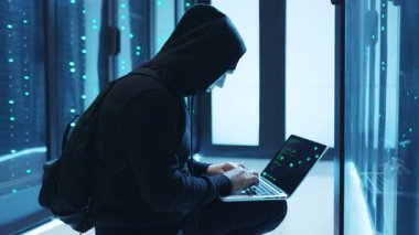 Loş, fütüristik bir ortamda, maske takan gizlenmiş bir figür gizlice dizüstü bilgisayarlarında çalışır.