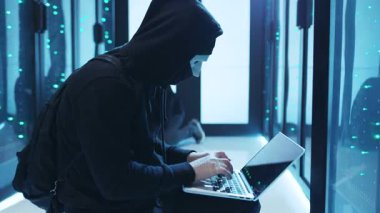 Gizemli bir kukuletalı figür, gelişmiş ekipmanlarla dolu yüksek teknoloji veri merkezinde gizlice bir dizüstü bilgisayar kullanıyor.