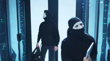 Siyah elbiseli ve çarpıcı beyaz maskeli iki gizemli figür zıt bir zemine karşı dururlar.