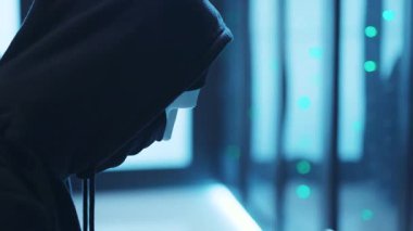 Modern bir ortamda kapüşonlu ve maskeli gölgeli bir karakter. Gizem ve anonimliği somutlaştırıyor..