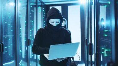 Loş bir sunucu odasında, gizemli maskeli bir şahıs parlayan sunucular arasında hackleme faaliyetleriyle meşgul.
