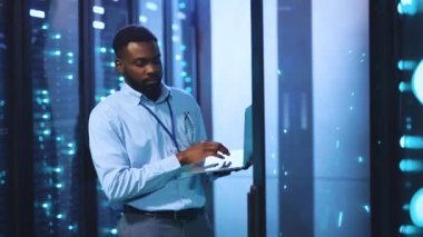 Odaklanmış bir adam sunucular ve yanıp sönen ışıklarla çevrili yüksek teknoloji sunucu odasında, veri sistemlerinde acil ve teknik uzmanlık gösteren bir laptop kullanır.