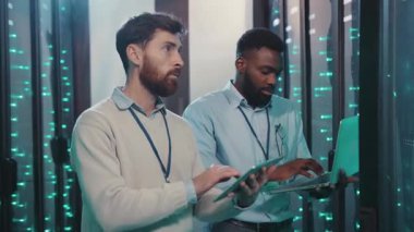 Yoğun bir sunucu odasında, iki profesyonel birlikte çalışıyor, bir tablet ve dizüstü bilgisayardaki verileri analiz ediyor, günümüz teknolojisiyle işbirliği gösteriyor