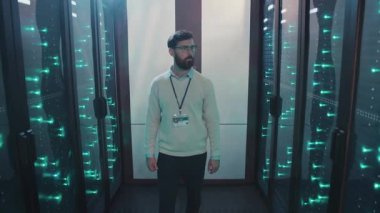 Bir adam sunucu odasının içinde duruyor. Çok sayıda sunucuyu ve teknolojiyi barındırmaya adanmış modern bir veri merkezinde.