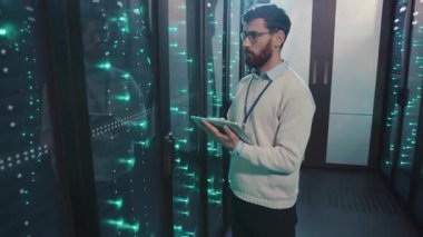 Bir adam yüksek teknoloji sunucu odasında bir tabletle ilgileniyor, bilgisayar sunucuları tarafından aydınlatılıyor, verileri analiz ediyor ve teknolojinin altyapıdaki rolünü vurguluyor