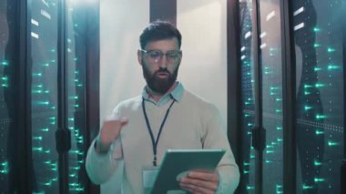 Sakallı bir adam yüksek teknoloji sunucu odasında ustaca geziniyor ve elinde tablet tutuyor. Acil hareketleri en iyi performansı sağlıyor.
