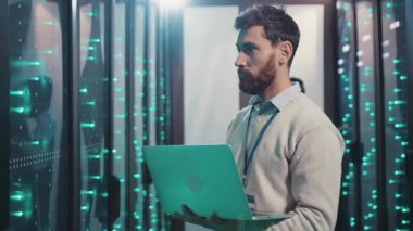 Bir adam bilgisayar için gerekli ekipman ve teknolojiyle dolu bir sunucu odasında güvenli bir şekilde dizüstü bilgisayar tutuyor.