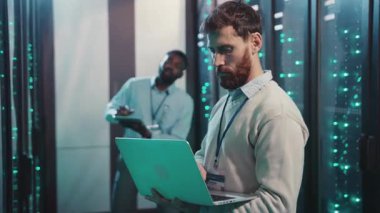 Bir sunucu odasında, iki profesyonel bir teknoloji projesinde işbirliği yapıyor. Biri dizüstü bilgisayar kullanırken, diğeri bir tablet üzerindeki bilgileri inceleyerek veri yönetimini geliştirir