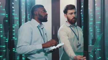 Yüksek teknolojili bir sunucu odasında, iki profesyonel veri ve sorun çözme sistemlerini analiz etmek için modern teknolojiyi kullanır, hızlı bir ortamda takım çalışması sergilerler.