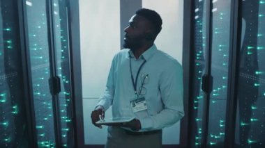 Yetenekli bir teknisyen yoğun bir sunucu odasında veri ve işlemleri izlemek için bir kulaklık ve tablet kullanarak sorunsuz performans sağlayarak çalışır.