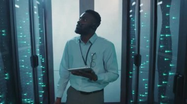 Bir adam sunucu odasında elinde tabletle dikiliyordu. Etrafı çok sayıda sunucu ve yüksek teknoloji ekipmanlarıyla çevriliydi.