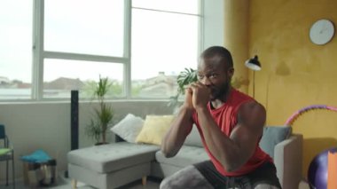 Formda bir adam, şık oturma odasında canlı kırmızı bir atletle çalışırken çevikliğini hula çemberiyle sergiliyor.