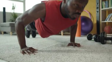 Kendini işine adamış bir adam, rahat bir oturma odasında şınav çeker ve fitness 'e bağlılığını gösterir. Sıcak atmosfer onun dürtüsünü ve rahatlığını arttırır.
