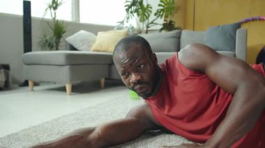 Bir adam, rahat bir oturma odasında çeşitli fitness egzersizleri yapar. Zemini esneterek esneklik ve şınav çekerek dayanıklılık gösterir.