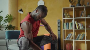 Bir adam rahat bir oturma odasında egzersiz yapıyor, ağırlık kaldırmak ve çömelmek gibi egzersizler için dambıl kullanıyor, fitness yolculuğunu vurguluyor.