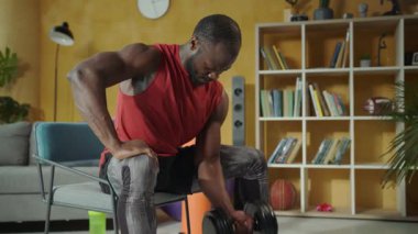 Konforlu bir oturma odasında, bir adam halter egzersizleri yapar, güç ve kararlılıkla spor yapmaya olan bağlılığını gösterir