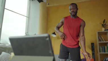 Bir adamın oturma odasında enerjik bir fitness seansı vardır. Kendine güvenerek tabletle çömelir. Kararlılık ve çok yönlülük gösterir.